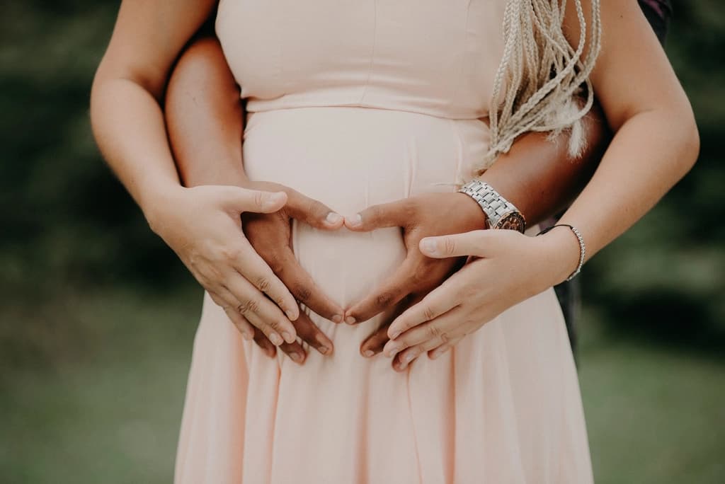 Mãos de um casal formando um coração sobre a barriga da gestante